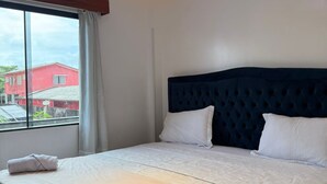 A hotel room with a large bed, a headboard, a window with curtains, and a ceiling light.