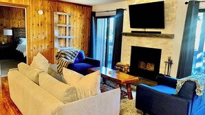 A living room with a sofa, armchairs, a coffee table, a fireplace, and a TV mounted on the wall. - Cozy Village Condo | Hot Tub, Sauna, Fireplace (Mammoth Lakes)
