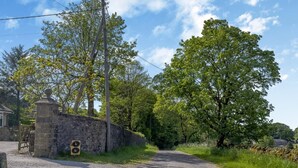 A rural road with a stone wall on one side and a large tree on the other. - 2 Bed in Buxton (oc-91974) (Wormhill)
