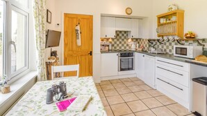 A compact kitchen with a dining area, a wooden door, a clock, and a window with curtains. - 2 Bed in Buxton (oc-91974) (Wormhill)