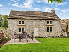 Une maison en pierre avec un toit en tuiles, une porte d’entrée et un petit jardin agrémenté d’une table et de chaises.