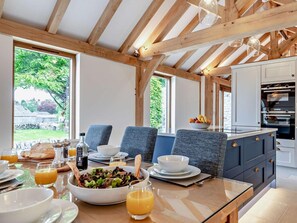 Une cuisine moderne avec des poutres en bois, un coin repas avec des chaises bleues et une vue sur le jardin.