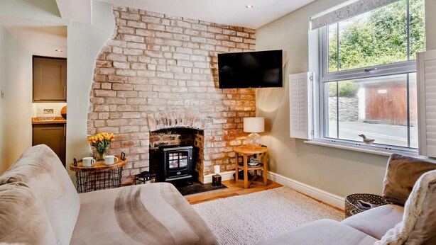 Una sala de estar acogedora con chimenea de ladrillo, televisor de pantalla plana montado en la pared, un sofá cómodo y un amplio ventanal con vistas al exterior.