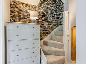 A staircase with a stone wall backdrop, a white dresser with gold knobs, and a lamp on top. - 3 Bed in Aberdovey (oc-92346) (Aberdovey)