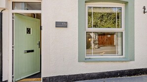 Un edificio de dos pisos con una puerta verde y una ventana con vistas a la vegetación.