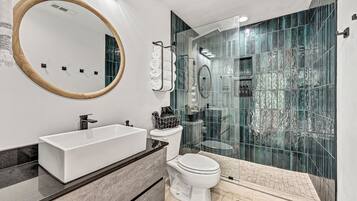 Un baño moderno con un espejo ovalado grande, un lavamanos rectangular, un inodoro y una zona de ducha con mampara de vidrio.