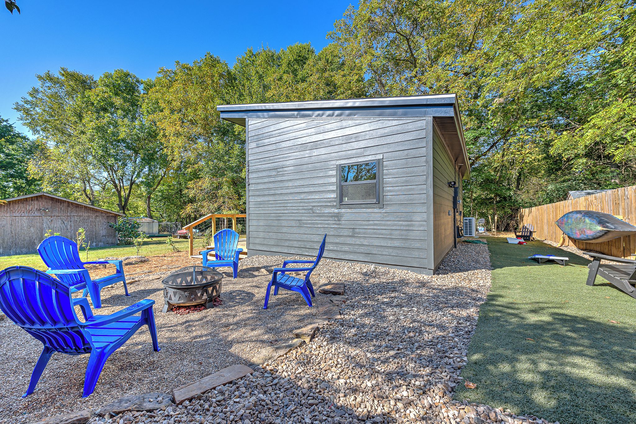 A small cabin with a window, surrounded by a gravel area with chairs and a fire pit.