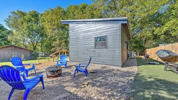 A small cabin with a window, surrounded by a gravel area with chairs and a fire pit.