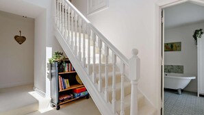 A staircase with white balusters, a bookshelf with books and decorative items, a heart-shaped wall decoration, and a glimpse of a bathroom with a bathtub and patterned floor. - 4 Bed in Alston (oc-92351) (Alston)