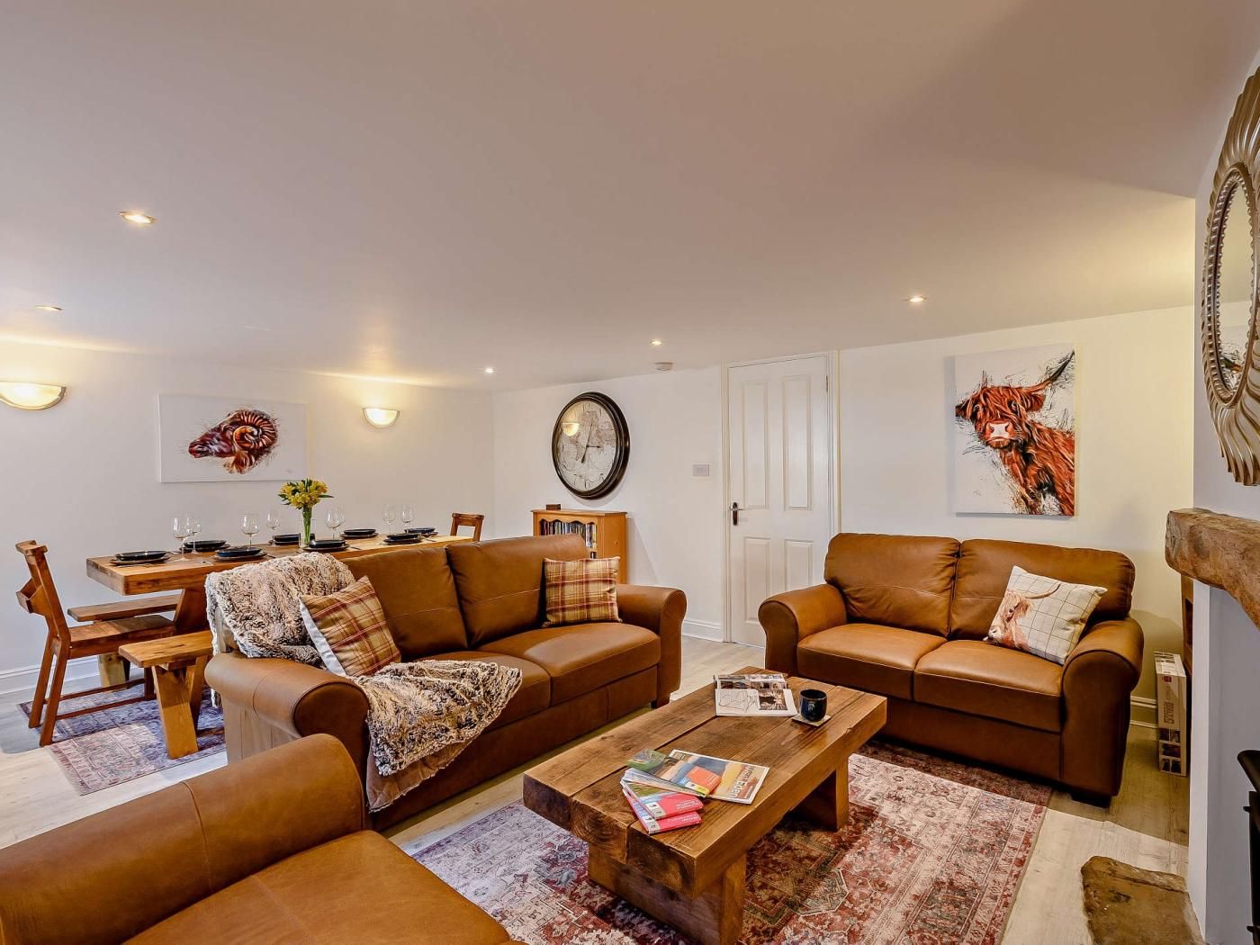 A living room with two brown leather sofas, a wooden coffee table, and a dining area with a wooden table and chairs.
