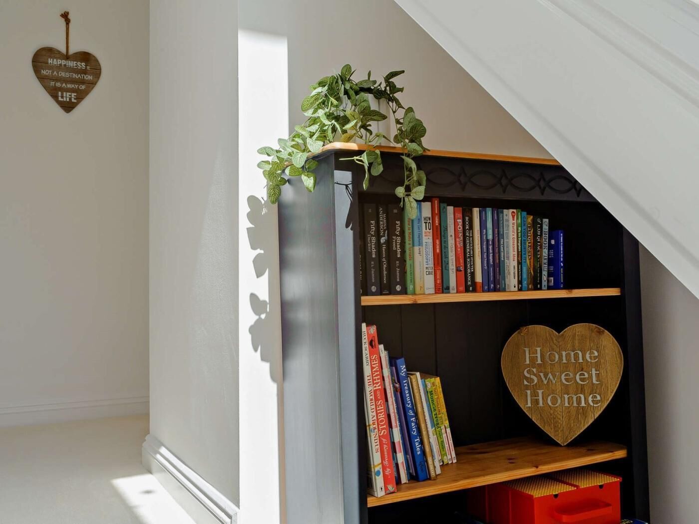 A bookshelf with books, a heart-shaped sign saying 'Home Sweet Home,' and a hanging plant.