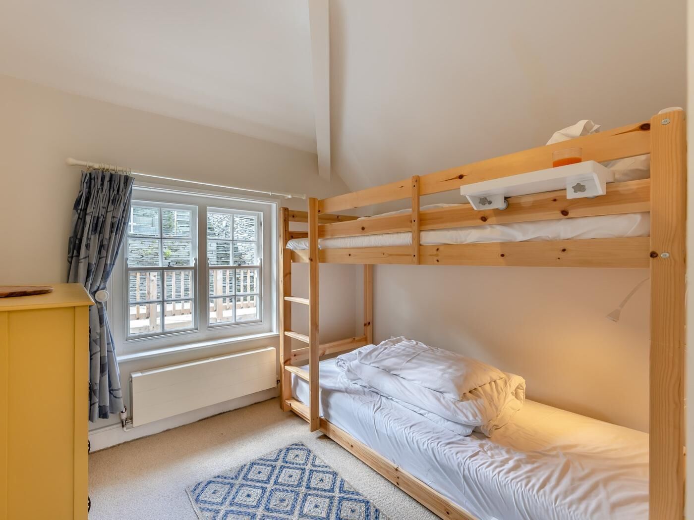 A bunk bed room with a window, a radiator, and a patterned rug.