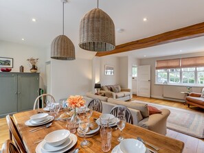 A dining area with a wooden table set for a meal, a sofa, and a window with blinds. - 3 Bed in Aberdovey (oc-91915) (Aberdovey)