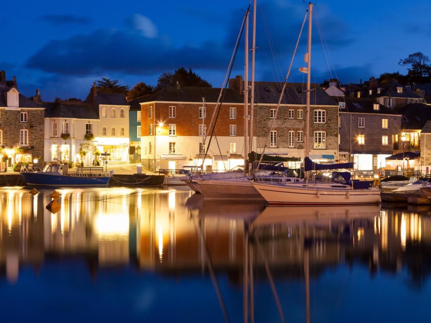 A waterfront town with buildings reflecting on calm water, boats docked, and a clear sky.