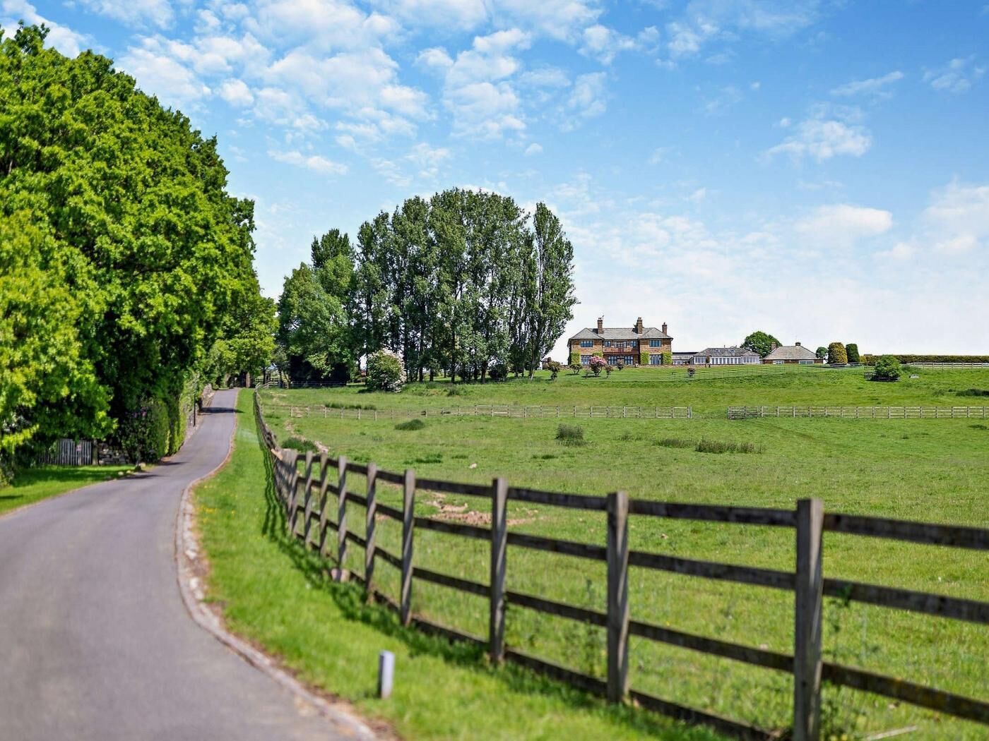 A rural road curving through a green landscape with a large house and open fields.