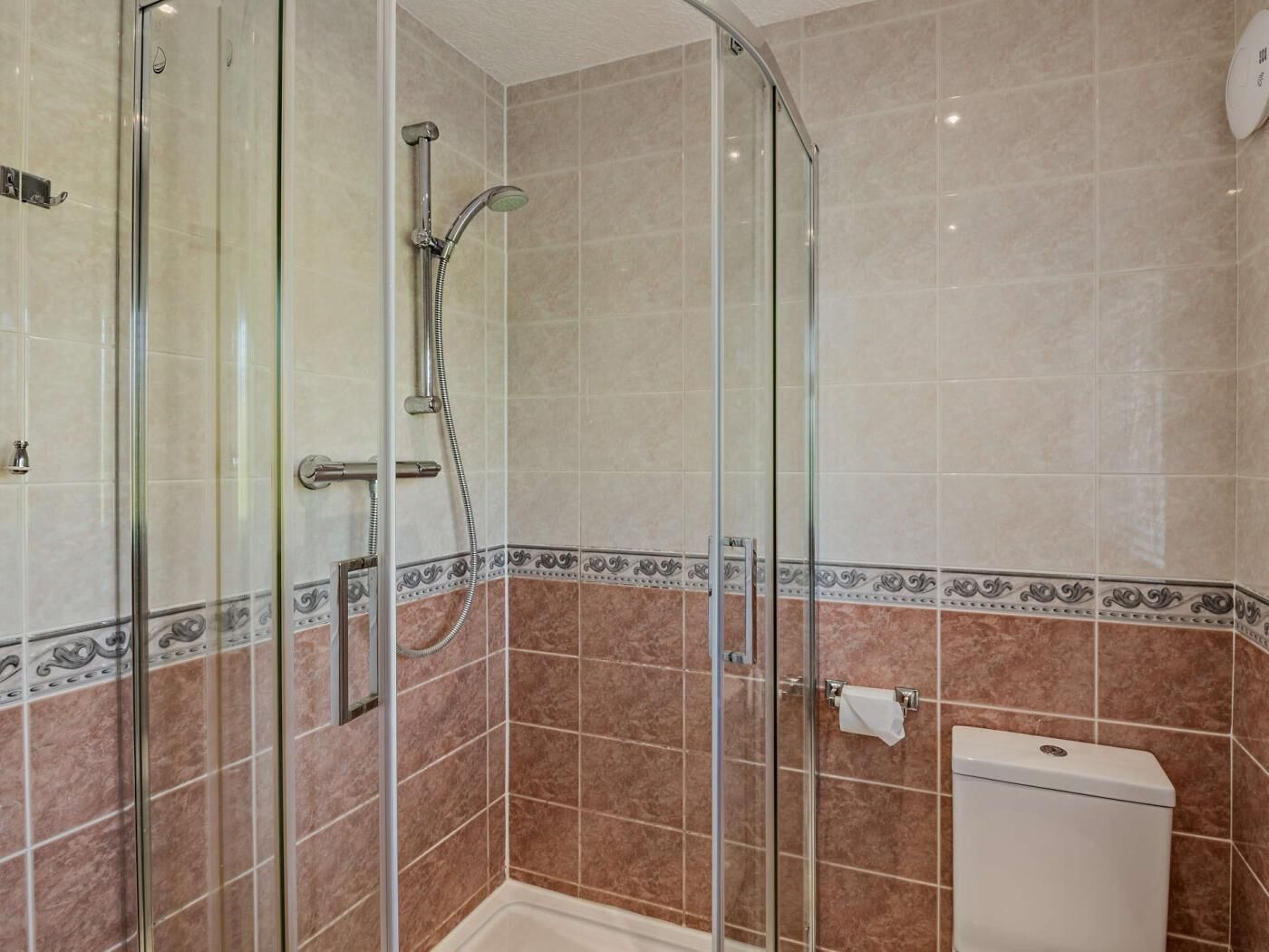 Une douche fermée par des parois en verre, dotée d’un pommeau de douche mobile, d’une porte en verre et de toilettes avec un porte-serviettes en papier.