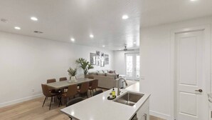 A spacious living area with a dining table, sofas, and a kitchen with a sink.