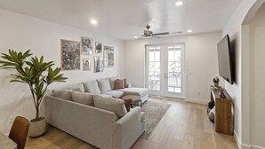 A living room with a sofa, a ceiling fan, a TV, and a door leading outside.
