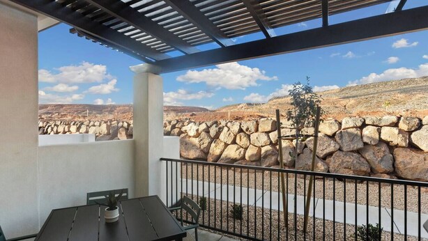 A balcony with a table and chairs, a stone wall, and a view of a rocky landscape.