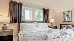 Quarto de hotel com uma cama, duas mesas de cabeceira, uma janela com cortinas, uma luminária e um quadro na parede.