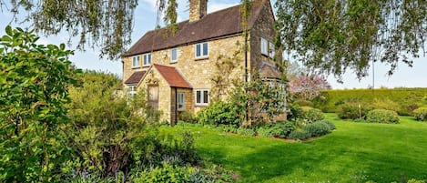 A stone house with a red roof, surrounded by a well-maintained garden with various plants and flowers.