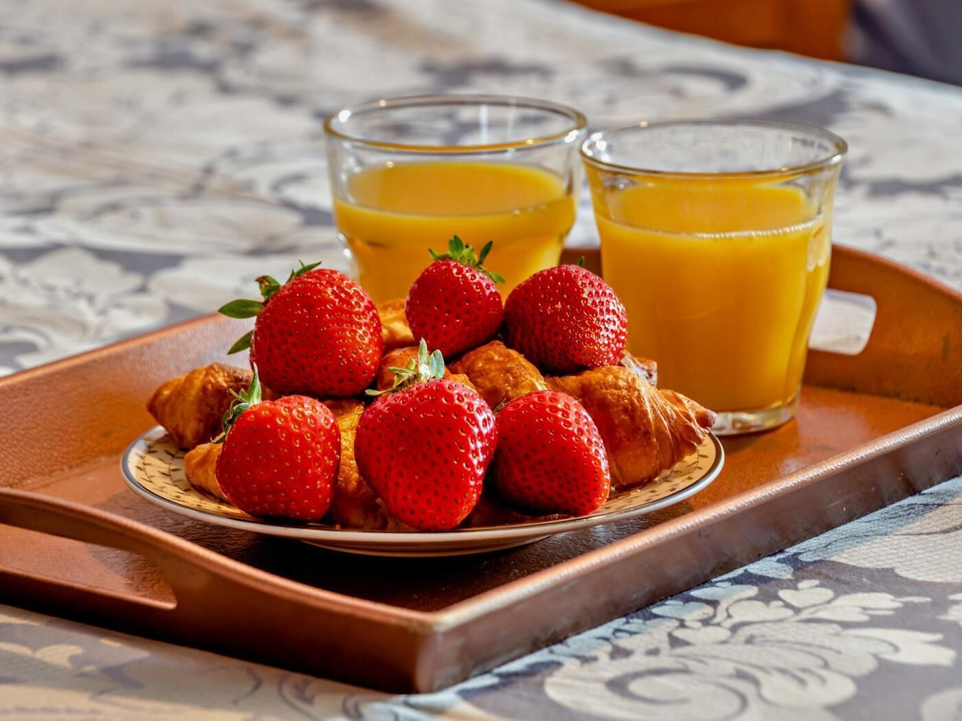 Un plateau avec des croissants, des fraises et deux verres de jus d’orange, posé sur une table.