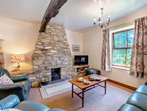 A cozy living room with a stone fireplace, leather furniture, a television, and a window with curtains. - 3 Bed in Pickering (oc-92356) (Cropton)