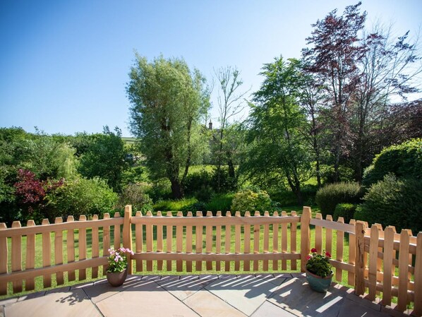 Une terrasse en bois avec une clôture à lattes, des plantes en pot et une vue sur un jardin luxuriant.