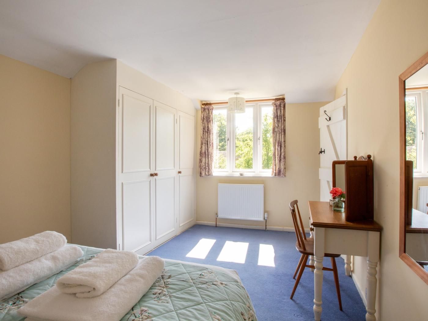 A bedroom with a bed, a desk, a chair, a radiator, and a window with curtains.