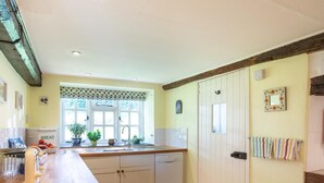 Eine Küche mit einer Holzarbeitsplatte, weißen Schränken, einem eingebauten Geschirrspüler und einem Fenster mit gemusterten Vorhängen.