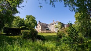 Ein traditionelles Steinhaus mit Strohdach, umgeben von üppiger Vegetation und einem gepflegten Rasen.