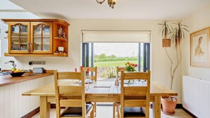 Een eetruimte met een houten tafel en stoelen, een keuken met houten kastjes, een raam met uitzicht en een kamerplant.