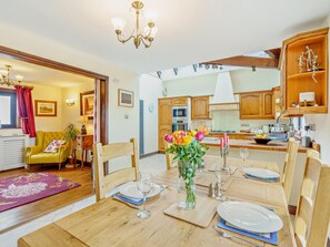 A dining area with a wooden table set for four, a vase with flowers, and a kitchen in the background. - 3 Bed in Preston (oc-92057) (Brindle)
