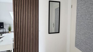 Une pièce moderne avec un séparateur en bois, un bureau blanc avec un ordinateur, un miroir et un mur gris à la texture intéressante.