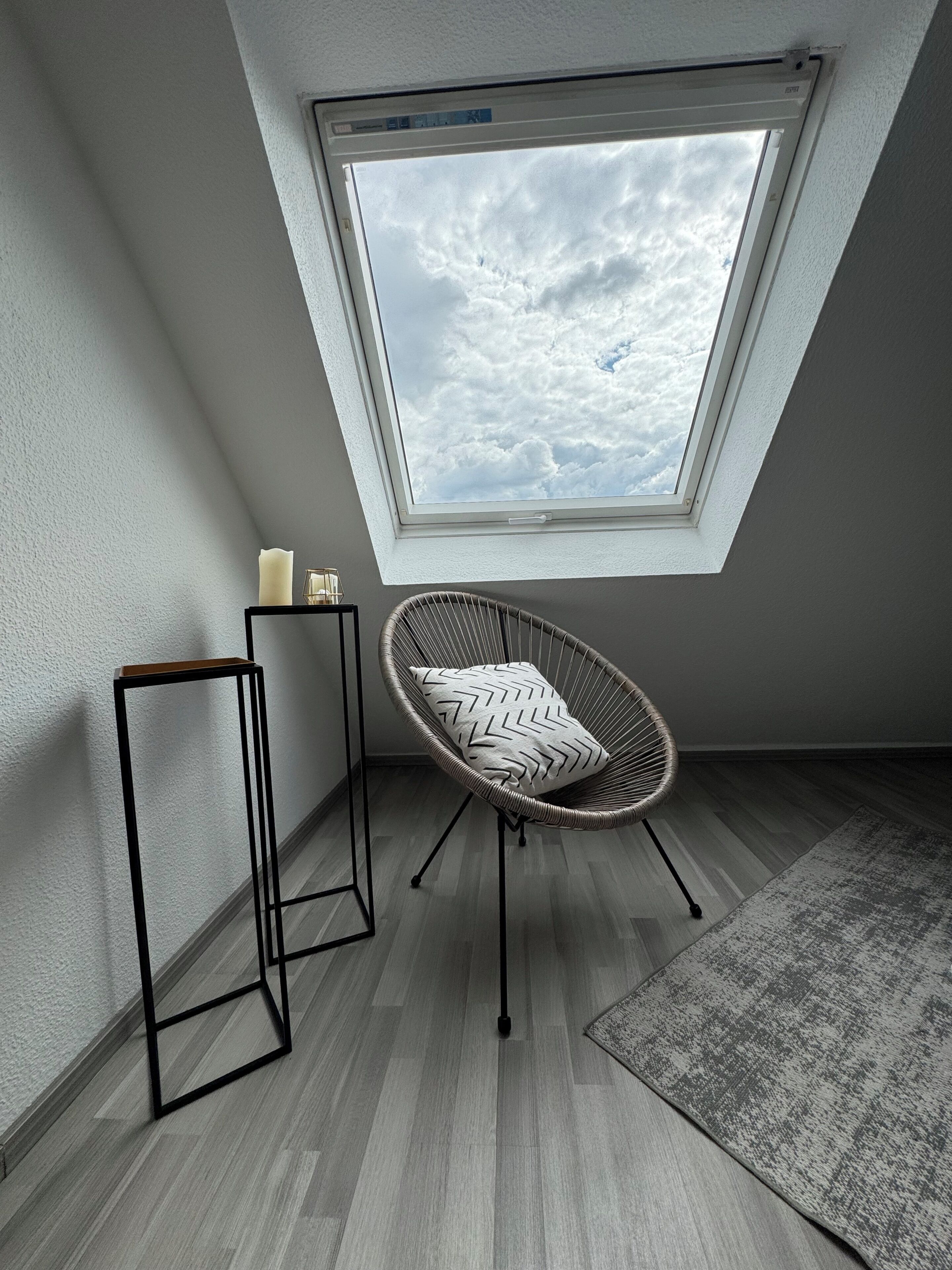 A room with a skylight, a chair, a small table, and a rug.