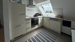 Une cuisine compacte dotée d’un puits de lumière, de meubles blancs et d’un tapis à rayures.