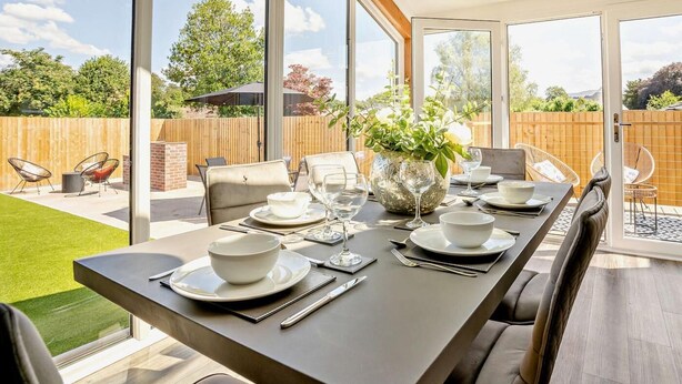 A dining area with a table set for four, large windows, and a view of a backyard.