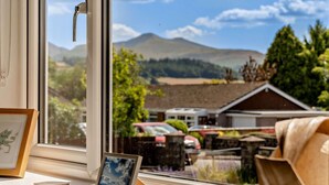 A window with a view of a mountain, a framed picture, and a small table with a picture frame and a coaster.