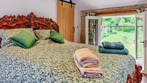 Een slaapkamer met een groot bed, een houten hoofdbord, een schuifdeur naar een tuin en een plafond met zichtbare balken.