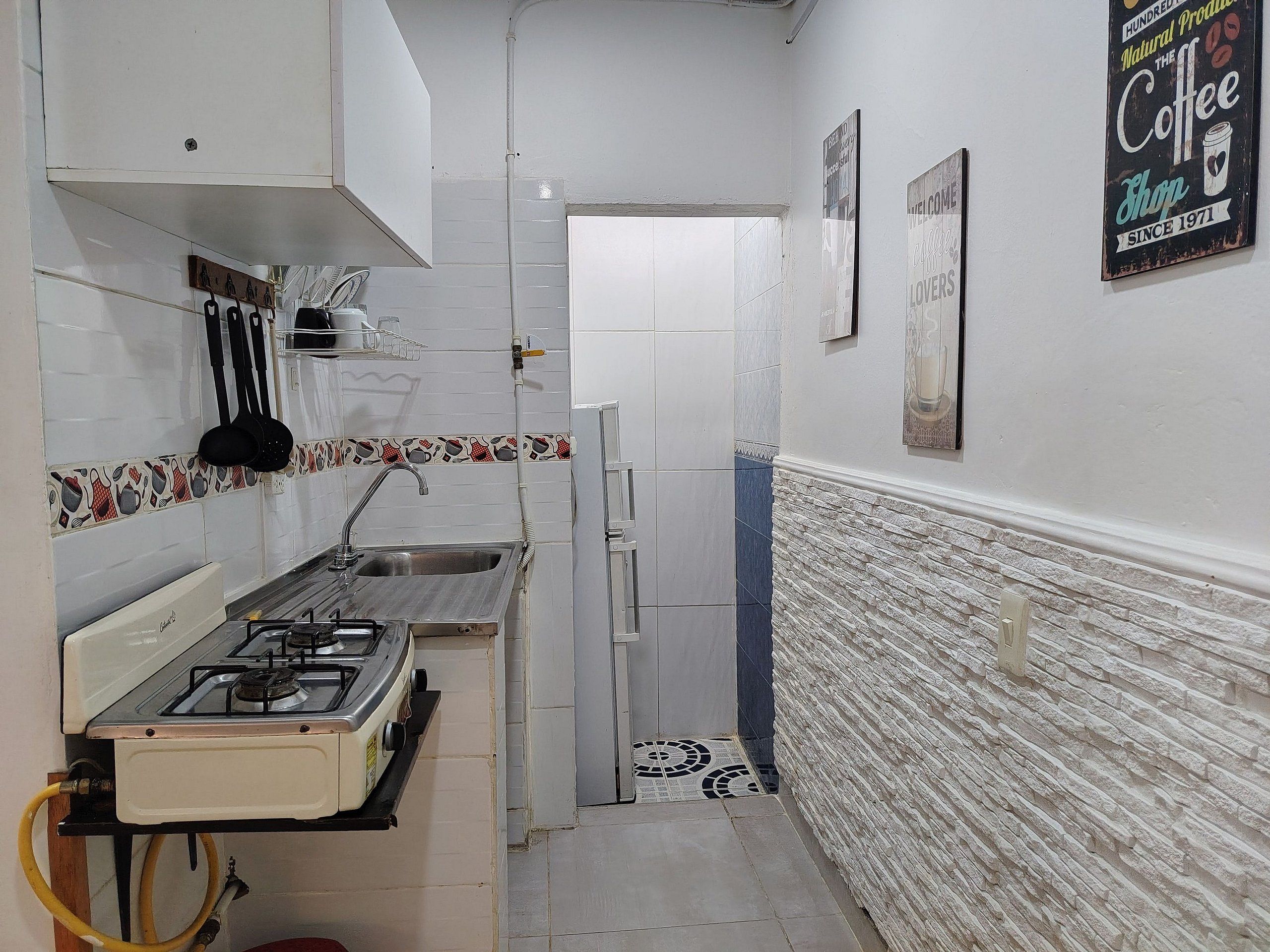 A narrow kitchen with a gas stove, sink, and tiled backsplash.