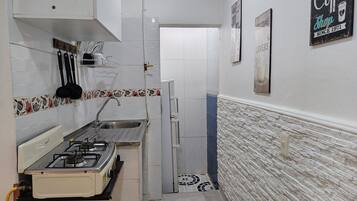 A narrow kitchen with a gas stove, sink, and tiled backsplash.