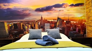 Uma cama com almofadas e um cobertor, vista para a cidade e uma parede de tijolos.