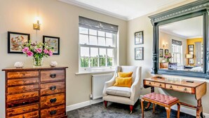 Une pièce comprenant une commode en bois, un fauteuil blanc, un bureau en bois et un grand miroir.
