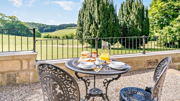 Un espace de restauration en plein air avec une table dressée pour le petit-déjeuner, comprenant du pain, une carafe de jus d’orange et un pichet.