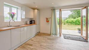 Une cuisine moderne avec des meubles blancs, un plan de travail en bois, un four à micro-ondes et une fenêtre agrémentée d’un vase de fleurs.