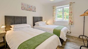 Une chambre double avec deux lits, une fenêtre ornée de rideaux à motifs floraux, un luminaire suspendu et un radiateur.