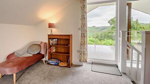 Une pièce chaleureuse avec un canapé, une bibliothèque en bois, une lampe et une vue sur un balcon.