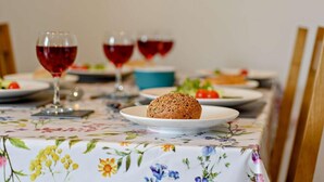 Une table à manger recouverte d’une nappe à motifs floraux, une assiette contenant une pâtisserie et des verres de vin rouge.
