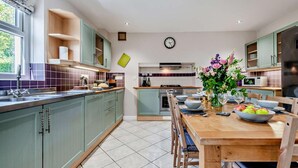 A modern kitchen with green cabinets, a wooden dining table, and a clock on the wall. - 3 Bed in Carmarthen (oc-92116) (Gwernogle)