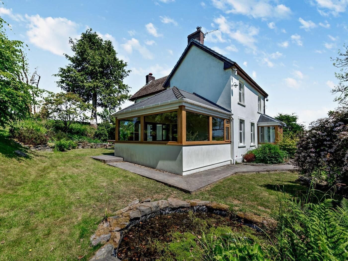 A two-story house with a conservatory, surrounded by a well-maintained garden and a small pond.